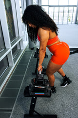 Woman in red athletic wear, loading a sport 24 attachment barbell with the adjustable dumbbells displaying the lock or locking system
