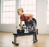 Woman exercising with the sport 24 adjustable dumbbells on a Nomad bench in a home gym setting