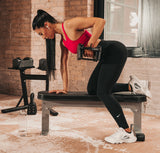 Woman exercising with the sport 24 adjustable dumbbells on a Nomad bench in a home gym setting