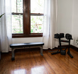 Home gym setup with the nomad weight bench and adjustable dumbbell rack in a bright room with large windows 