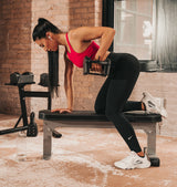 Woman exercising with the sport 24 adjustable dumbbells on a Nomad bench in a home gym setting