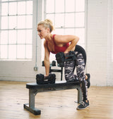 Woman exercising with the sport 24 adjustable dumbbells on a Nomad bench in a home gym setting