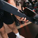 Hands adjusting the PowerBench 2.0 frame in a home gym with dumbbells in the background